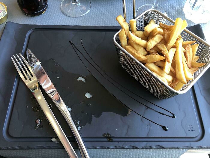 French fries served in a metal basket with fork and knife on a black placemat showcasing clever overlooked solutions.