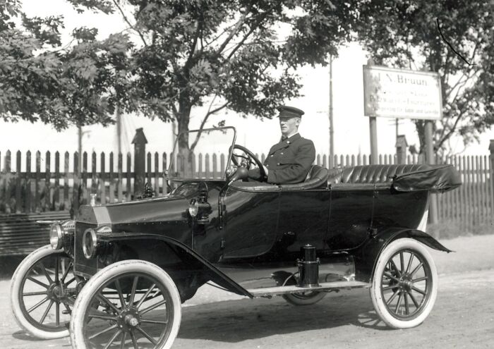 Man in uniform driving a vintage car, showcasing historic commutes and early 20th-century working world transport.
