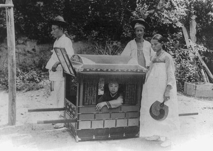 Historic commute scene showing traditional Korean palanquin carried by workers with a passenger inside in a bygone working world.