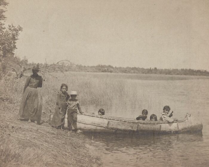 Historic commutes shown with children boarding a wooden canoe by a lakeshore in a bygone working world setting.
