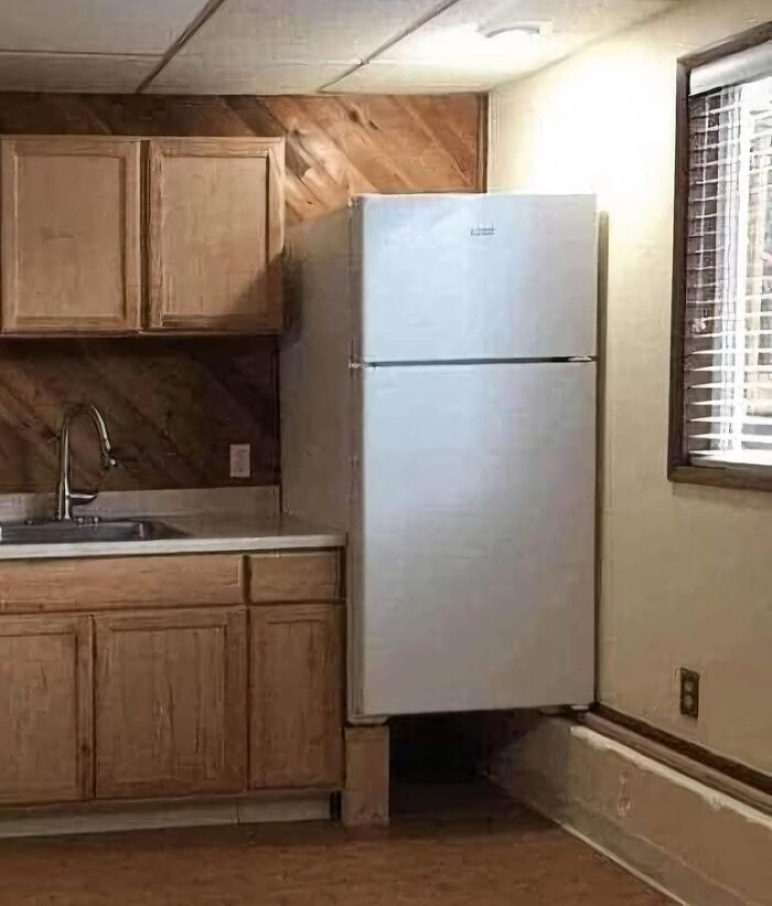 Poorly designed kitchen with a white refrigerator awkwardly elevated, showcasing one of the worst real estate photos ever.