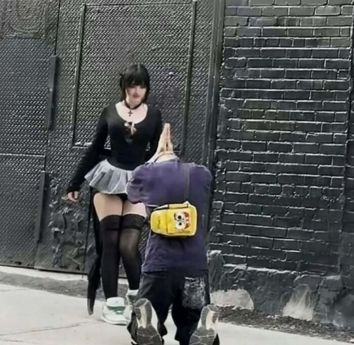 Person kneeling to take a photo of a girl in edgy clothing, capturing cringey pictures on an urban sidewalk.
