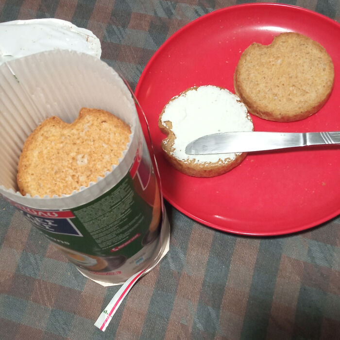 Round crackers with missing bites shown in a packaging tube and spread with cream cheese on a red plate, clever food solution.