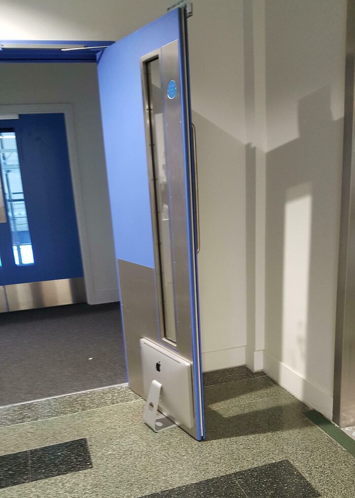 A tall blue door is humorously propped open by an iMac computer, showcasing a funny tech fail setup.