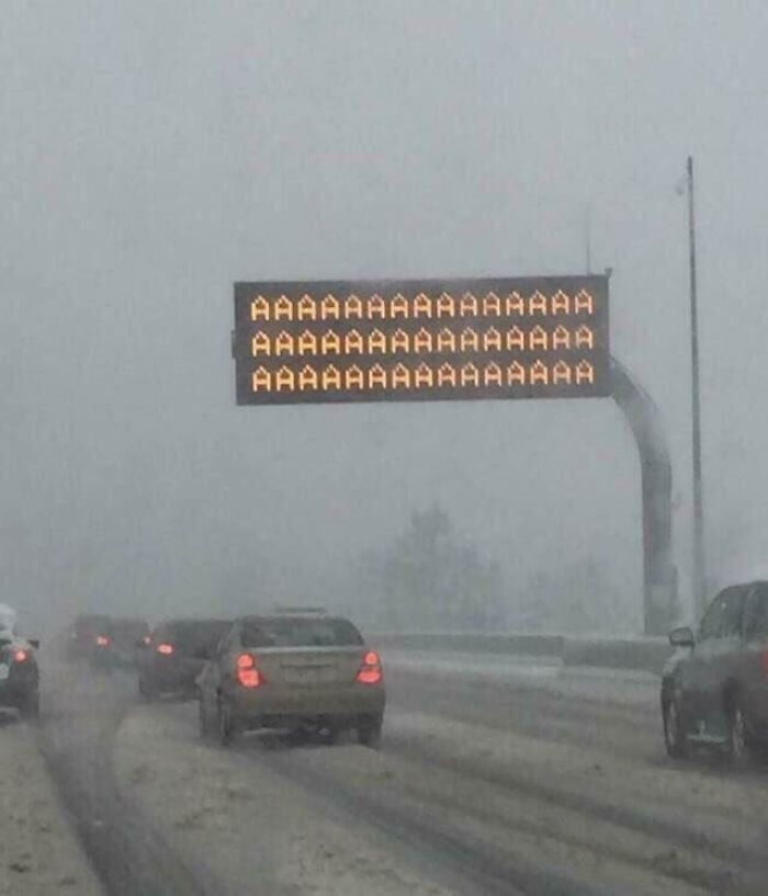 Highway electronic sign showing repeated letter A during snowy weather, a hilarious tech fail on a busy road.