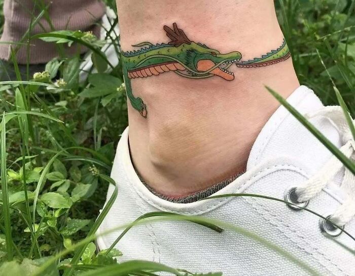 Tatuaje de dragón verde alrededor del tobillo, ejemplo de personas que decidieron hacerse tatuajes divertidos y llamativos.