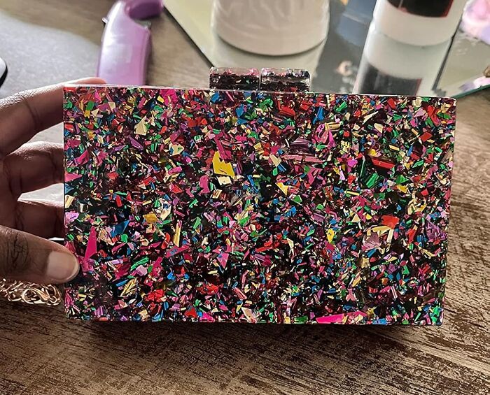Colorful and glittery clutch purse held by a hand, showcasing one of the weirdly wonderful finds vibrant and unique accessories.