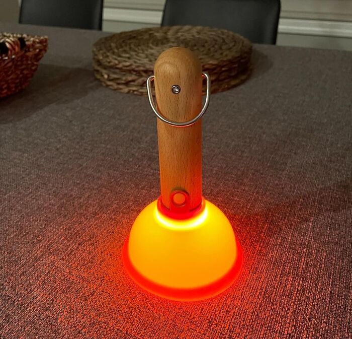 Orange glowing plunger with wooden handle on a textured table as a weirdly wonderful find for beige-loving friends.