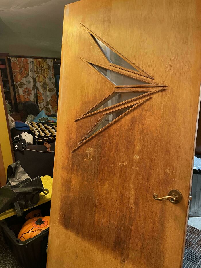 Wooden mid-century door with geometric glass design and brass handle in a vintage-style interior setting.