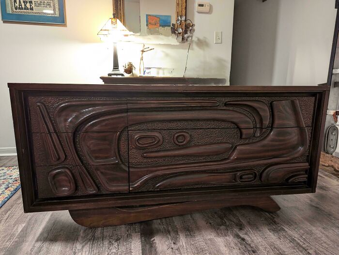 Mid-century vintage wooden sideboard with intricate carved design in a cozy room with lamp and mirror.