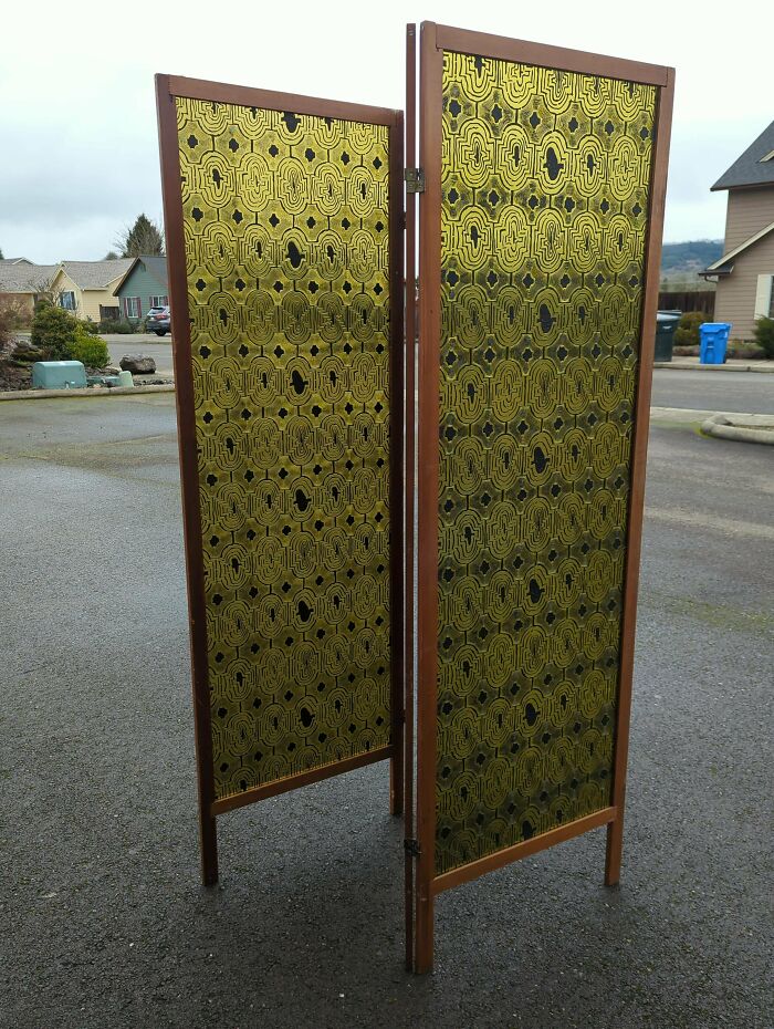 Mid-century room divider with vintage patterned gold and black panels and wooden frames standing outdoors on pavement.