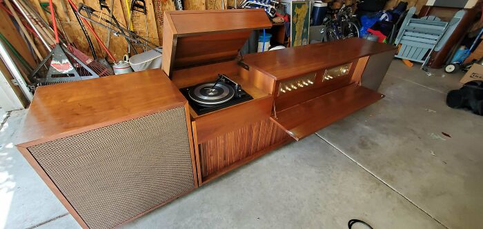 Mid-century design vintage wooden record player console with speakers in a garage setting showing retro charm.