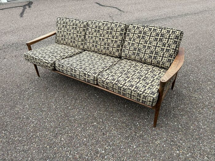 Mid-century design wooden framed sofa with patterned cushions showcasing effortless vintage charm on pavement.