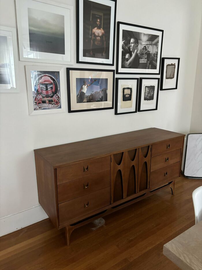 Mid-century designs wooden sideboard with curved details against white wall displaying framed vintage art prints.