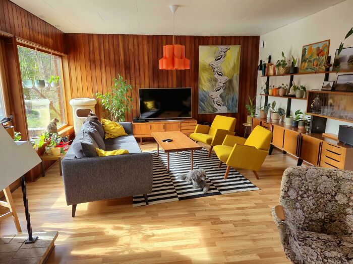 Mid-century designs living room with wood panel walls, yellow armchairs, gray sofa, and vintage decor accents.
