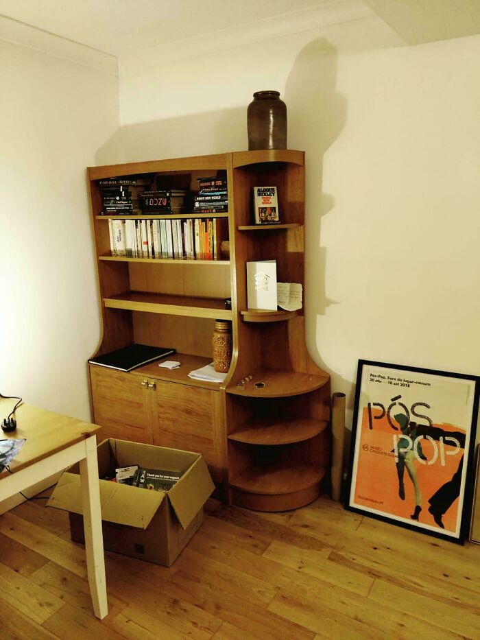 Mid-century designs wooden bookshelf with vintage decor, books, and a framed retro poster on a hardwood floor room.