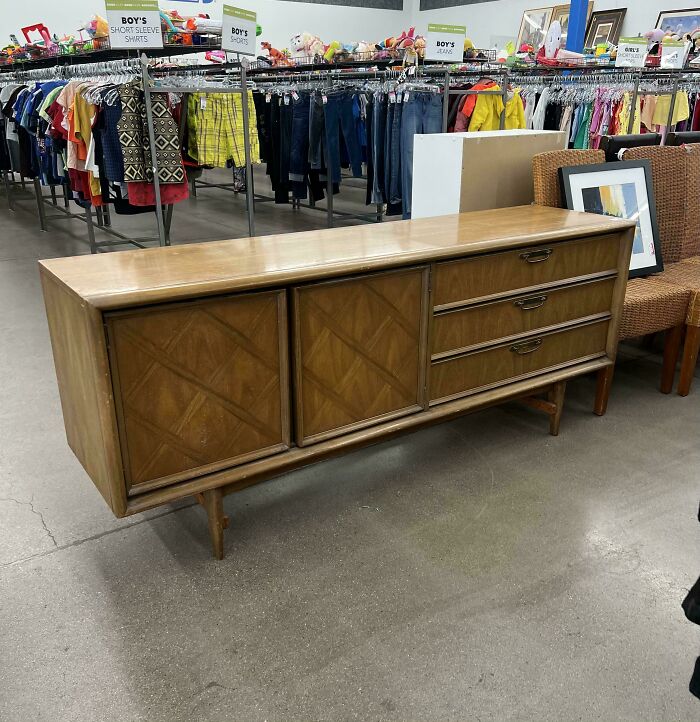 Mid-century wooden sideboard with drawers and sliding doors, showcasing vintage charm and classic design in a thrift store setting.