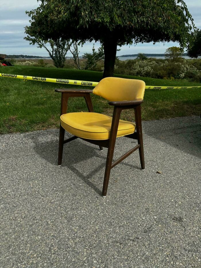 Mid-century design chair with yellow cushion and wooden frame sitting outdoors near caution tape.