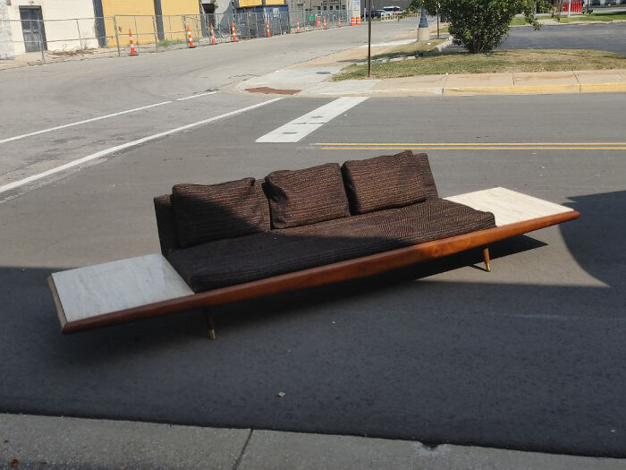 Mid-century vintage sofa with dark cushions and wooden frame placed outdoors on pavement, showcasing effortless vintage charm.