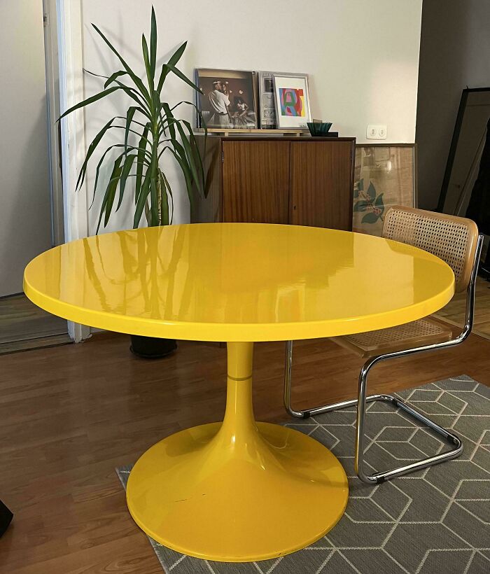 Yellow mid-century modern round table paired with a cane chair in a vintage-inspired living space.