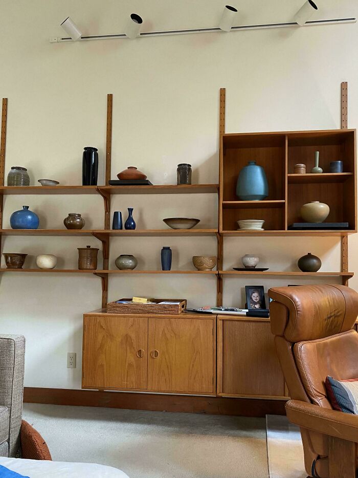 Mid-century design wooden shelving unit with vintage pottery and decor in a cozy living room setting.