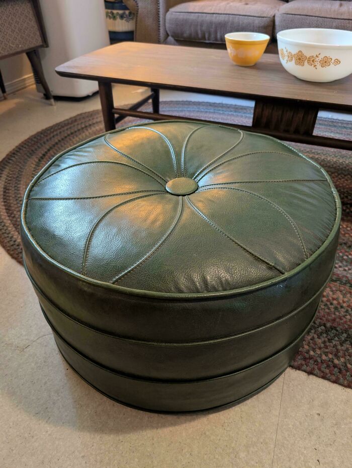 Green leather round ottoman with stitched design in a mid-century living room featuring vintage furniture and decor.