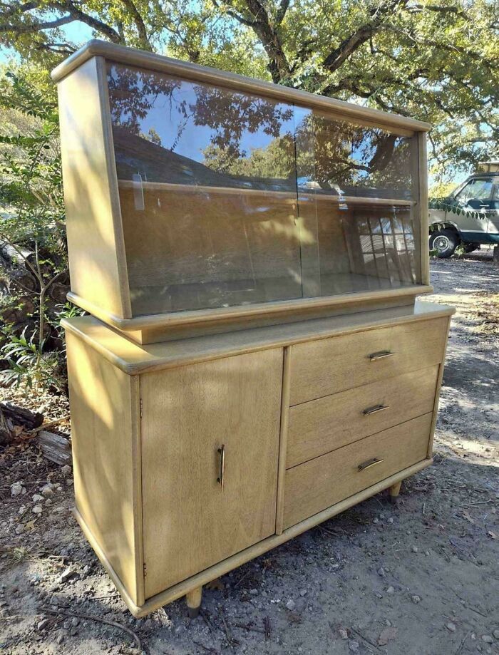 Mid-century design wooden cabinet with glass display and drawers, showcasing effortless vintage charm in an outdoor setting.
