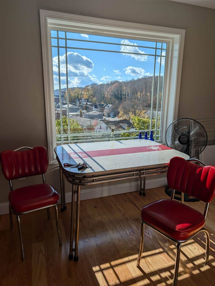 Mid-century designs featuring a vintage diner table and red chairs in sunlight by a large window with outdoor view.