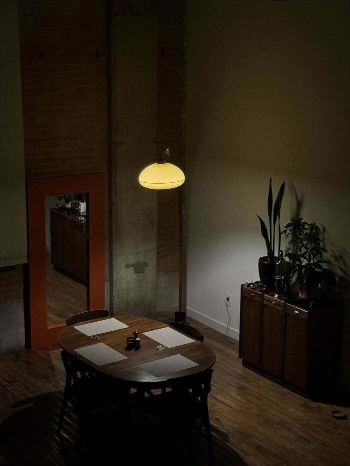 Dimly lit dining area featuring mid-century designs with a wooden table, chairs, and vintage style pendant light above.