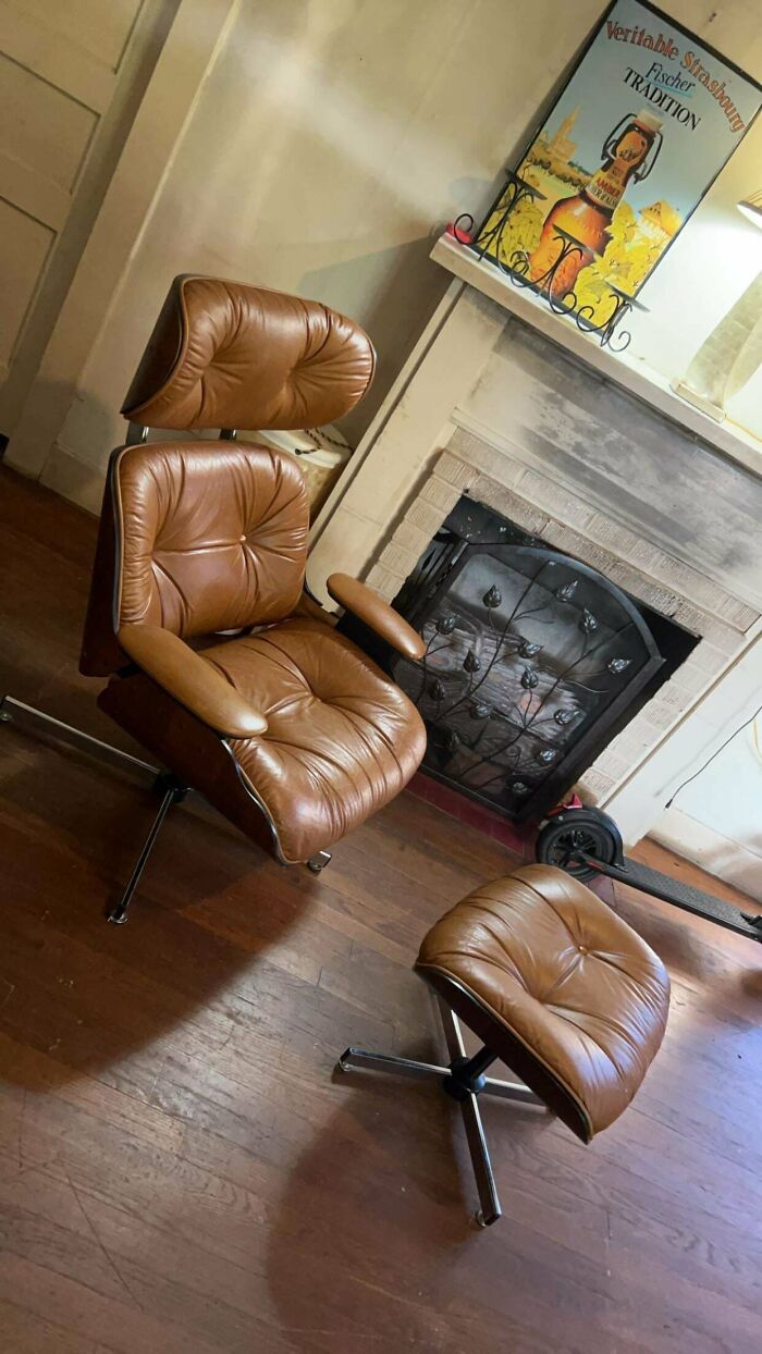 Mid-century leather lounge chair and ottoman in front of a vintage-style fireplace with decorative metal screen.