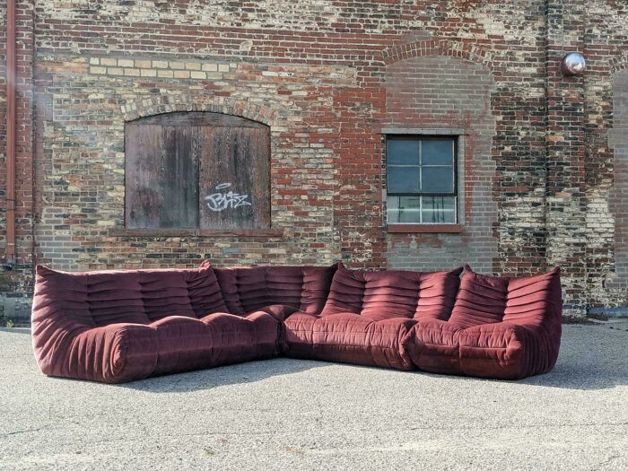 Mid-century design featuring a deep burgundy vintage sectional sofa set against a rustic brick wall background.