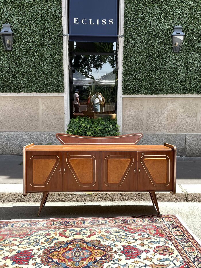 Mid-century vintage wood sideboard with geometric design, set outdoors against a green ivy wall and patterned rug.