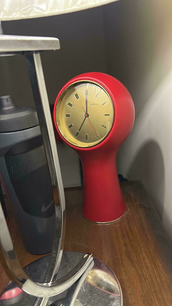 Red mid-century design clock with vintage charm on wooden surface beside a black water bottle and metallic lamp base.