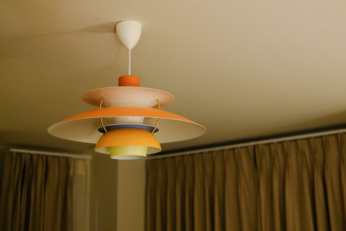 Mid-century designs ceiling lamp with layered shades in warm tones hanging above beige curtains in a vintage-inspired room.