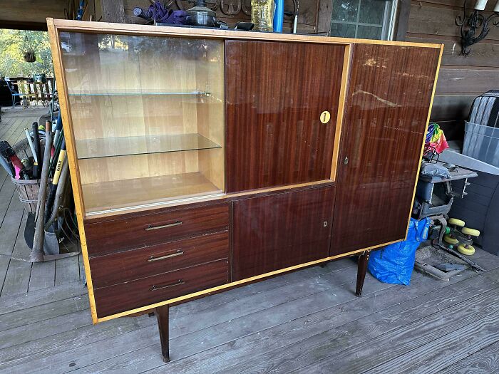 Mid-century vintage wooden cabinet with glass shelving and drawers, showcasing effortless vintage charm on a wooden porch.