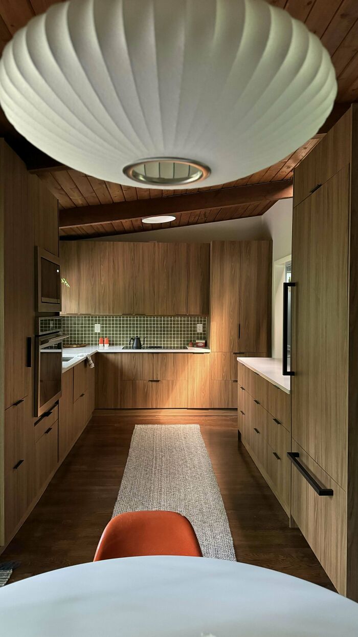Mid-century kitchen design featuring wood cabinetry, white countertops, modern light fixture, and vintage-inspired tiled backsplash.