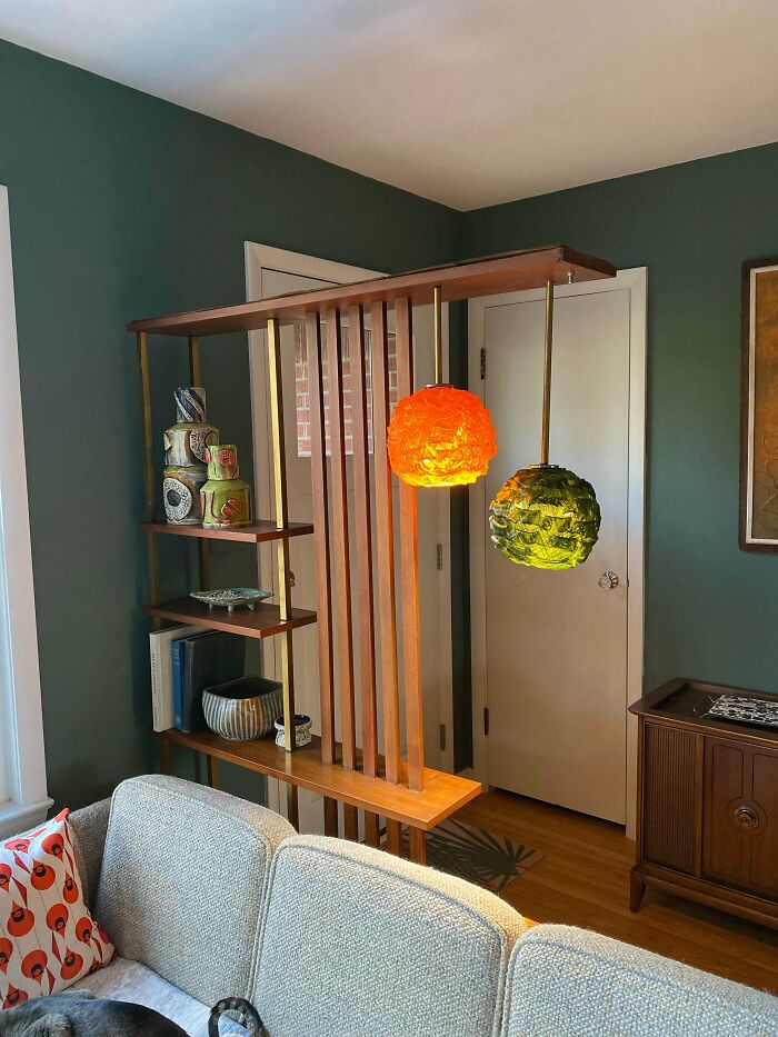 Mid-century room divider with vintage hanging lamps and wooden shelves displaying retro decor in a cozy living space.