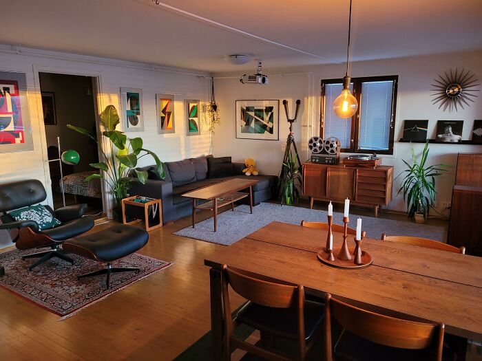 Mid-century living and dining room with vintage furniture, abstract wall art, plants, and warm ambient lighting.