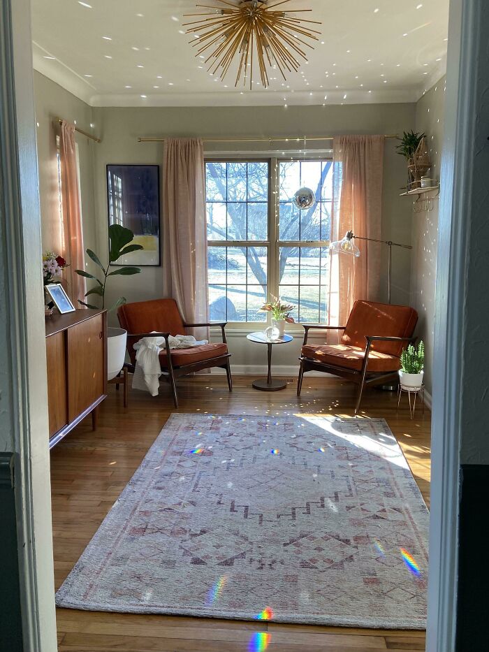 Sunlit mid-century living room with vintage armchairs, patterned rug, wooden furniture, and a starburst chandelier.