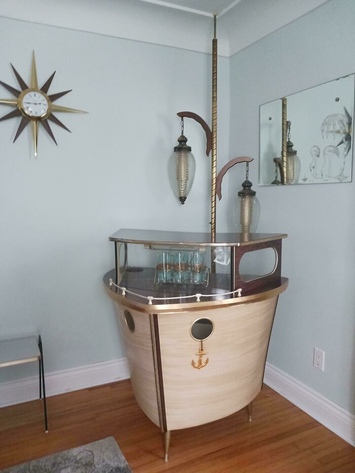 Mid-century vintage bar cart with nautical design, glassware, decorative clock, and hanging pendant light in stylish room.