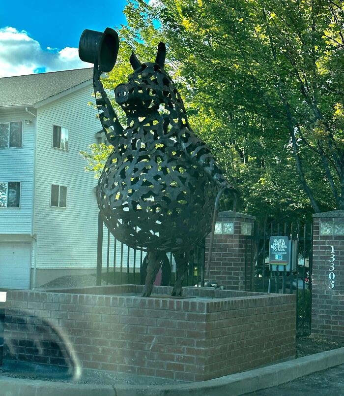 Large metal rooster sculpture tipping its hat in front of a residential building, highlighting infuriating landlords' unusual features.