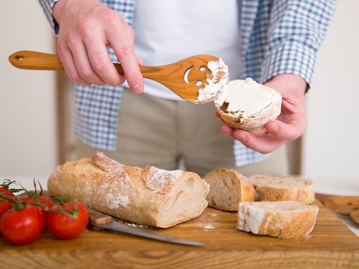Person spreading cream cheese on a bagel using a funny kitchen gadget with a smiling face design.