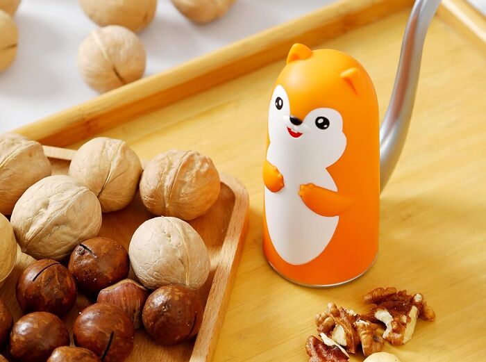 Funny kitchen gadget shaped like an animal cracking nuts, surrounded by whole and shelled walnuts on a wooden tray.
