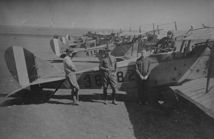 Three men standing beside and inside vintage planes lined up on an airfield, capturing the magic of aviation history.
