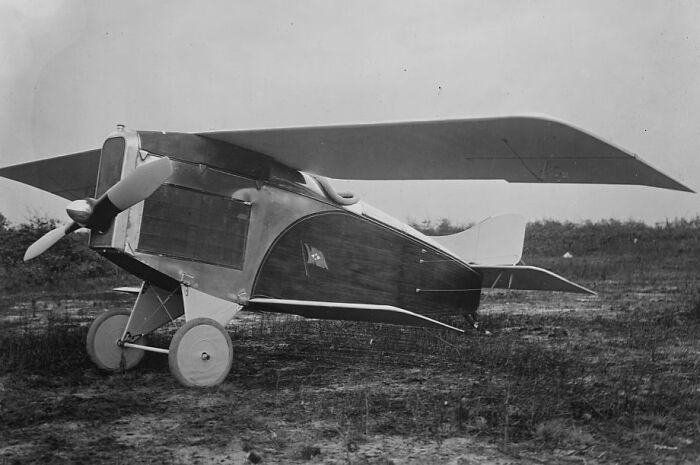 Vintage plane with wooden body and fabric wings resting on grass, showcasing early aviation design and technology.