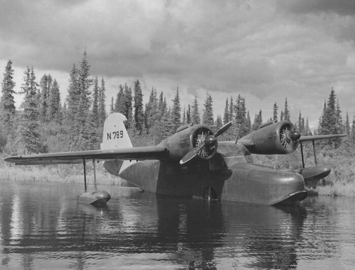 Vintage plane with twin propellers resting on water near a forest, capturing the magic of aviation history.