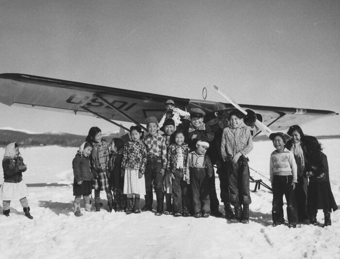 Group of children and adults standing in snow near a vintage plane, capturing the magic of aviation history.