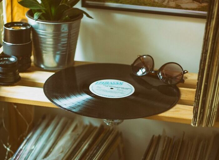 Vinyl record and sunglasses on wooden shelf with vintage camera and plant, reflecting Gen X lifestyle and culture.