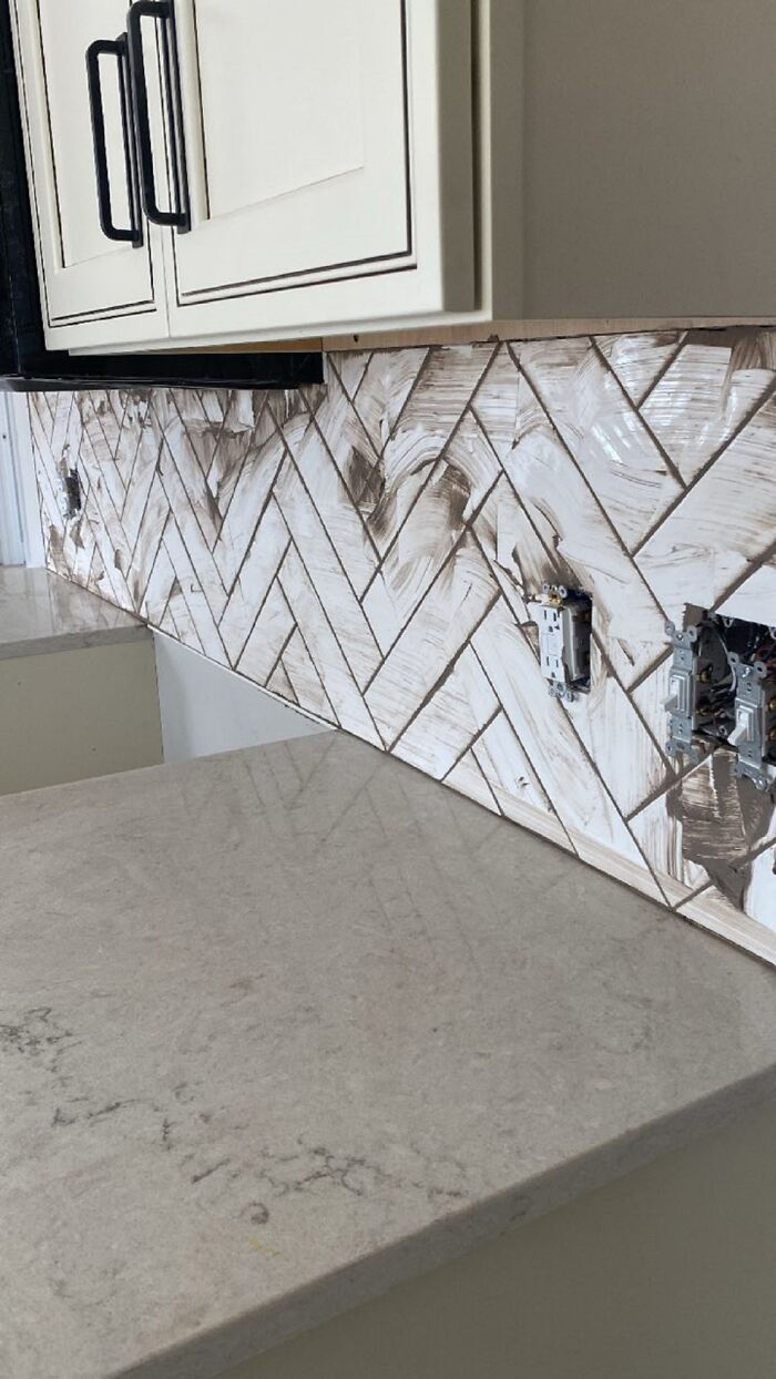 Kitchen backsplash tiles installed with visible messy grout and unfinished electrical outlets showing unexpected fails in home renovation.