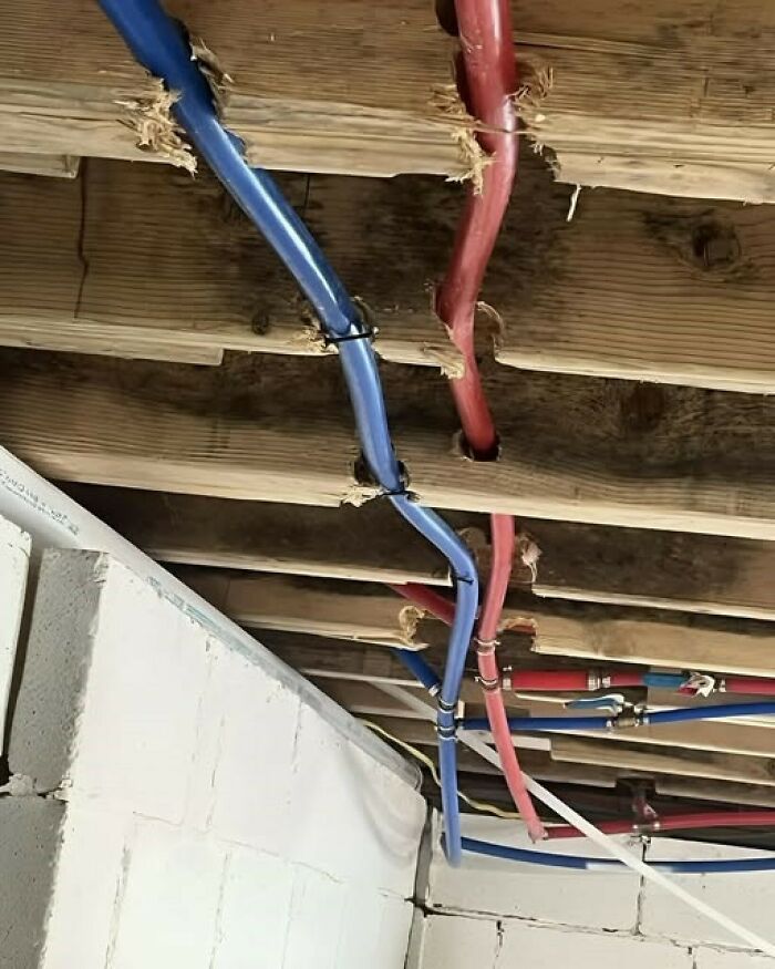 Blue and red pipes poorly installed through wooden beams, causing damage and illustrating unexpected fails in construction work.